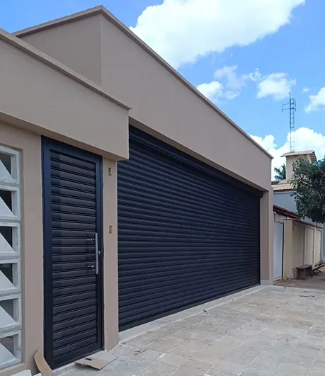 Residência com porta de enrolar preta e porta social metálica